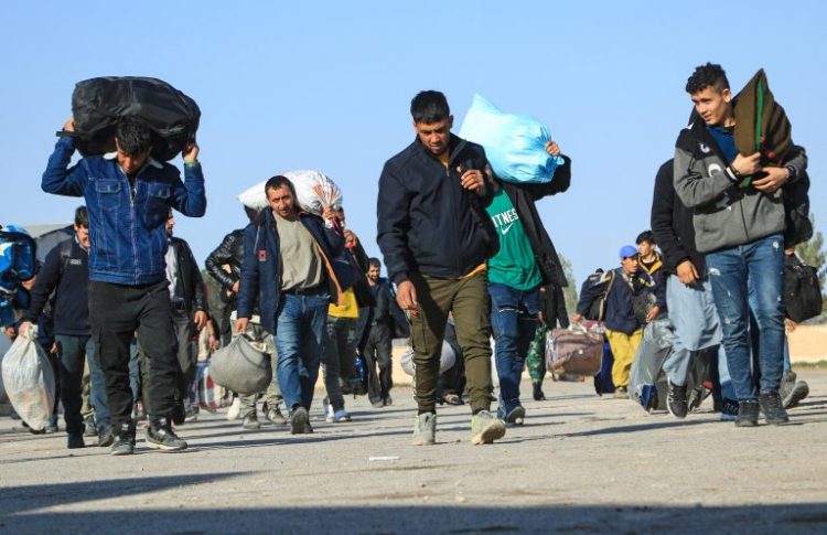 Afghan migrants carrying their belongings as they walk together, likely during a relocation or deportation process. (Photo Credit:Mohsen KARIMI / AFP)