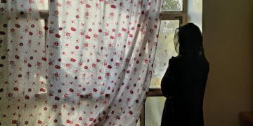 Women wearing black cloth staring from window outside.