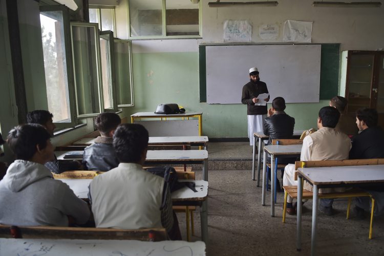 A teacher stands in a classroom, holding a paper and engaging with students, highlighting the enduring dedication to education in challenging times. (AFP)