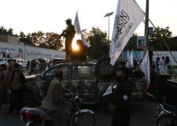 A Taliban ranger patrols through a bustling Kabul square, accompanied by armed militants, highlighting the group's presence in urban settings. (Photo Credit: Wakil KOHSAR / AFP)