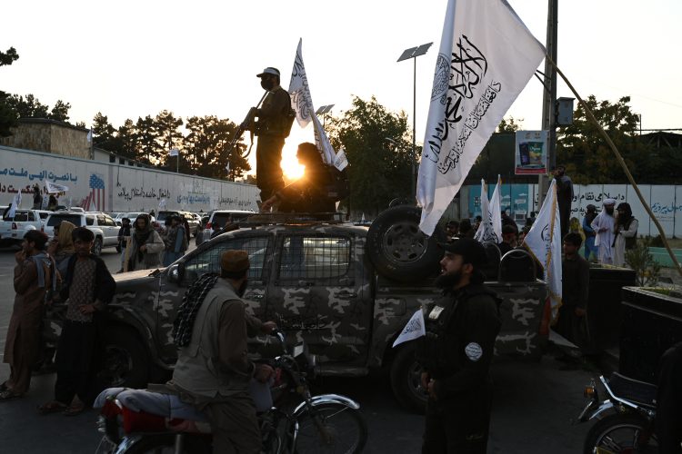 A Taliban ranger patrols through a bustling Kabul square, accompanied by armed militants, highlighting the group's presence in urban settings. (Photo Credit: Wakil KOHSAR / AFP)