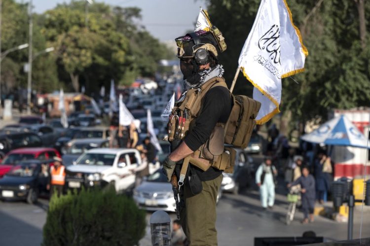A Taliban fighter in uniform stands in an Afghan square, the group's flag on his back. (Photo Credit: AFP)