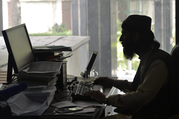 A Taliban fighter works on a desktop computer in a dimly lit room, highlighting their use of media as a propaganda tool. (Photo Credit: Ahmad SAHEL ARMAN / AFP)