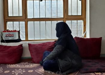 An Afghan woman gazes out of her home, reflecting the isolation and challenges faced by women in Afghanistan under Taliban rule. (Photo Credit: 8am.media)