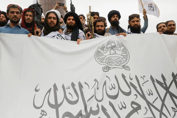 Taliban fighters hold a flag for the Islamic Emirate of Afghanistan in August 2022. (Photo Credit: Ali Khara/Reuters)