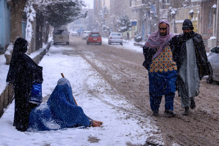 Amid heavy snowfall in Afghanistan, a woman with her children begs on a snowy street, reflecting the harsh realities of widespread poverty and economic struggles. (Photo Credit: Mohsen KARIMI / AFP)