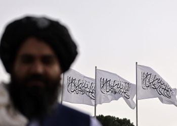 A Taliban official in focus against the backdrop of white Taliban flags, symbolizing the regime's authority. (Photo Credit: AFP)