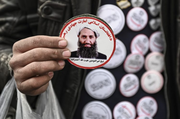 A person's hand holds a badge featuring the photo of the Taliban Supreme Leader. (Photo Credit: AFP)