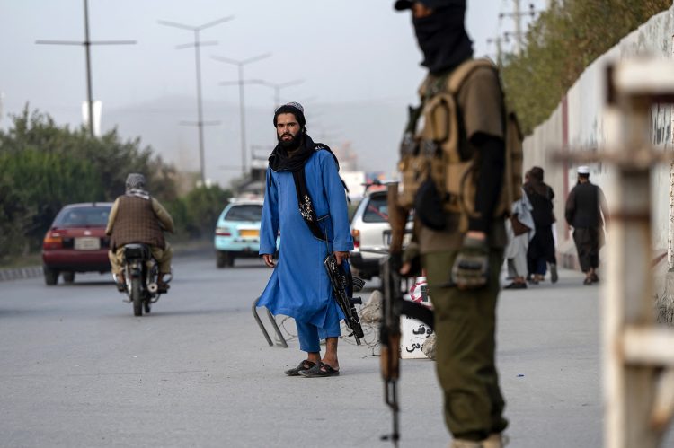Two Taliban fighters stand guard in Herat, western Afghanistan—one in uniform and the other in civilian attire—as internal conflicts within the group's ranks continue to escalate. (Photo Credit: Wakil KOHSAR / AFP)