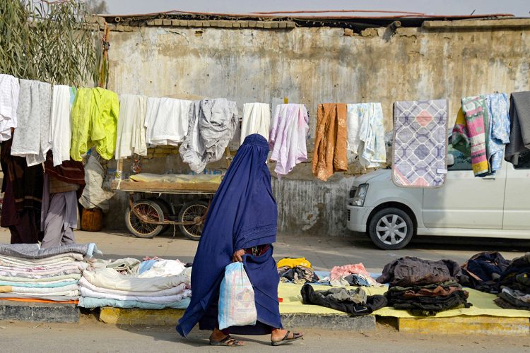 An Afghan woman in a burqa passes by a local market with clothes and linens drying under the sun. (Photo Credit: Sanaullah SEIAM / AFP)