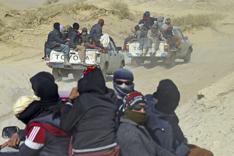 Groups of people travel through a rugged desert terrain, crowded in the back of pickup trucks, a common mode of transport in remote areas. In this picture taken on February 17, 2022, Afghan (Photo Credit: Wakil KOHSAR / AFP)