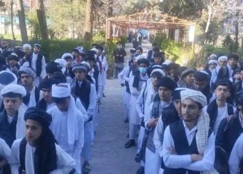 Taliban students in uniform, including white shirts, trousers, and headscarves, walking in line at a school in Afghanistan.