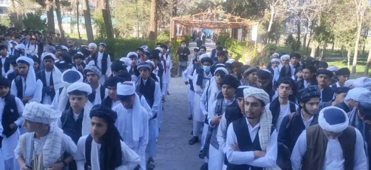 Taliban students in uniform, including white shirts, trousers, and headscarves, walking in line at a school in Afghanistan.