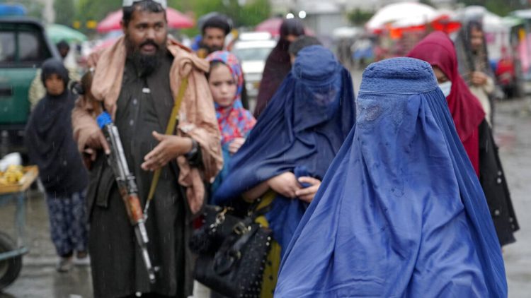 Afghan women walk past an armed Taliban fighter in Kabul as restrictions on their rights and freedoms continue to intensify. (Photo Credit: AP)