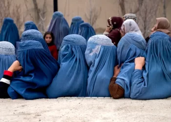 Afghan women in full-body blue burqas sit together as they await humanitarian aid distribution in Kabul. The re-imposition of strict Taliban policies has forced many women into public invisibility and deepened their reliance on emergency assistance. (Photo Credit: AFP)