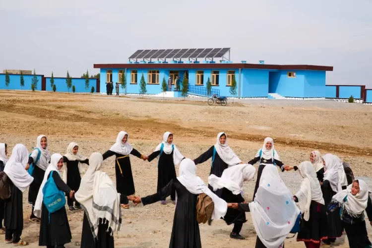 Afghan schoolgirls in black uniforms and white headscarves play joyfully in the schoolyard — a place once full of learning and laughter, now holding memories of an education left unfinished. (Photo Credit: UNICEF/UNI755231/Fazel)