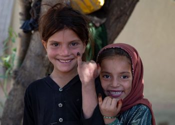 Two young Afghan girls smile after receiving their polio vaccines, proudly displaying their ink-marked fingers—a symbol of protection and hope in Afghanistan’s ongoing fight to eradicate polio. Photo Credit: PolioFreeAfghan