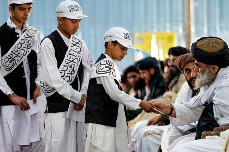 Taliban religious school students, dressed in uniforms bearing Islamic slogans, attend a graduation ceremony where a young boy receives a certificate from a senior Taliban official. (Photo Credit: AFP)