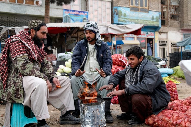 Street Vendors in Afghanistan warm themselves by a fire amidst a bustling market. (Photo Credit: AFP)