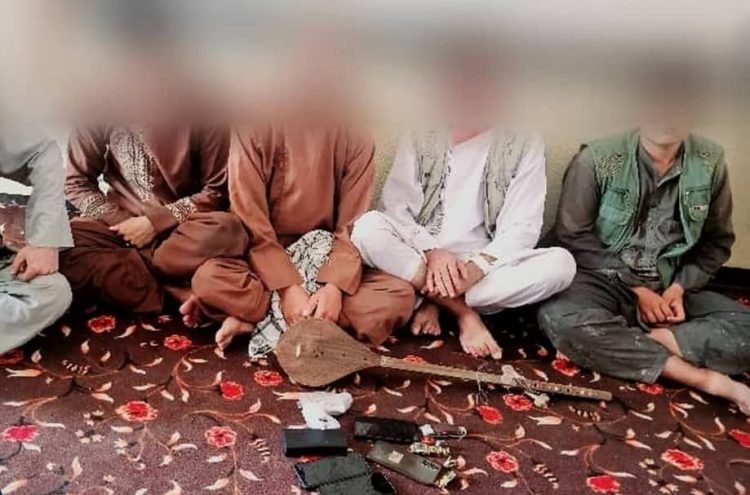 Five individuals sit on the floor with musical instruments, including a drum and a stringed instrument, in what appears to be a detained setting. (Photo Credit: Exclusive)