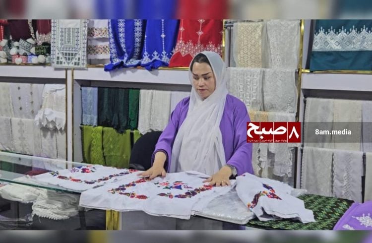 A woman arranges intricately embroidered textiles in a shop, showcasing traditional craftsmanship used for dowries in Afghanistan. (Photo Credit: 8am.media)
