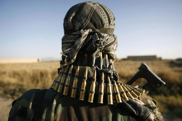 A Taliban fighter stands guard in a rural area, adorned with ammunition and a rifle, symbolizing the ongoing military presence. (Photo Credit: Reuters)