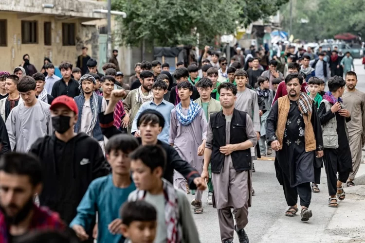 A large crowd of people, including many young men and boys, walks through a street in Afghanistan, reflecting the country's youthful population. (Photo Credit: AFP)