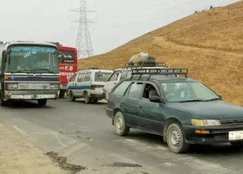 A congested road in Afghanistan shows a mix of vehicles, including a heavily loaded bus and a car with cargo on its roof, highlighting challenging road conditions. (Photo Credit: Ebrahim Mahdavi/DW)