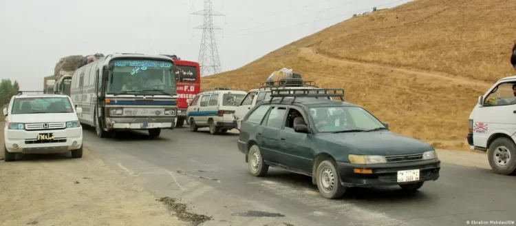 A congested road in Afghanistan shows a mix of vehicles, including a heavily loaded bus and a car with cargo on its roof, highlighting challenging road conditions. (Photo Credit: Ebrahim Mahdavi/DW)
