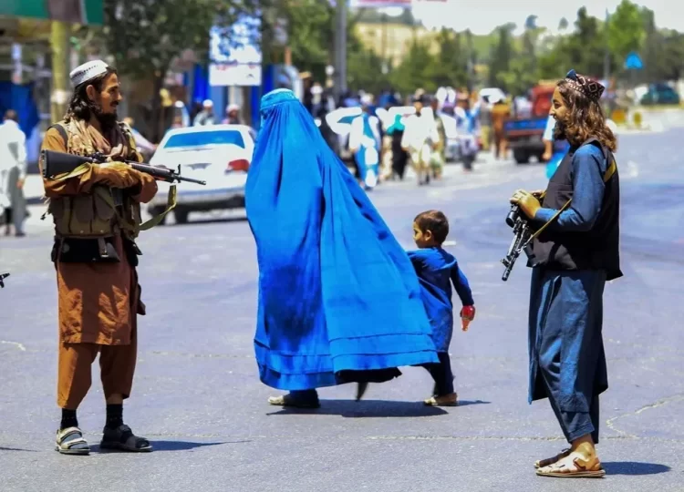Taliban fighters patrol a street in Kabul as a woman in burqa walks with a child, illustrating the heavy militant presence and restrictions on citizens' daily lives described in recent reports of harassment and intimidation. (Photo Credit: United Nation)