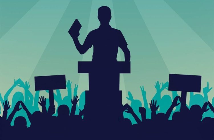 A silhouette of a speaker addresses a crowd holding signs at a political rally, symbolizing the democratic opposition's efforts to build unity and find common ground in Afghanistan's political future. (Photo Credit: International Monetary Fund)