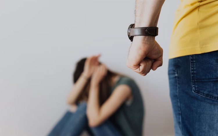 A man clenches his fist in a threatening pose over a distressed woman covering her face, illustrating the fear and intimidation in domestic abuse situations. (Photo Credit: AXA.com)