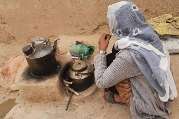 A woman in traditional clothing tends to cooking pots on the ground in a village in Afghanistan. (Photo Credit: Al Jazeera)