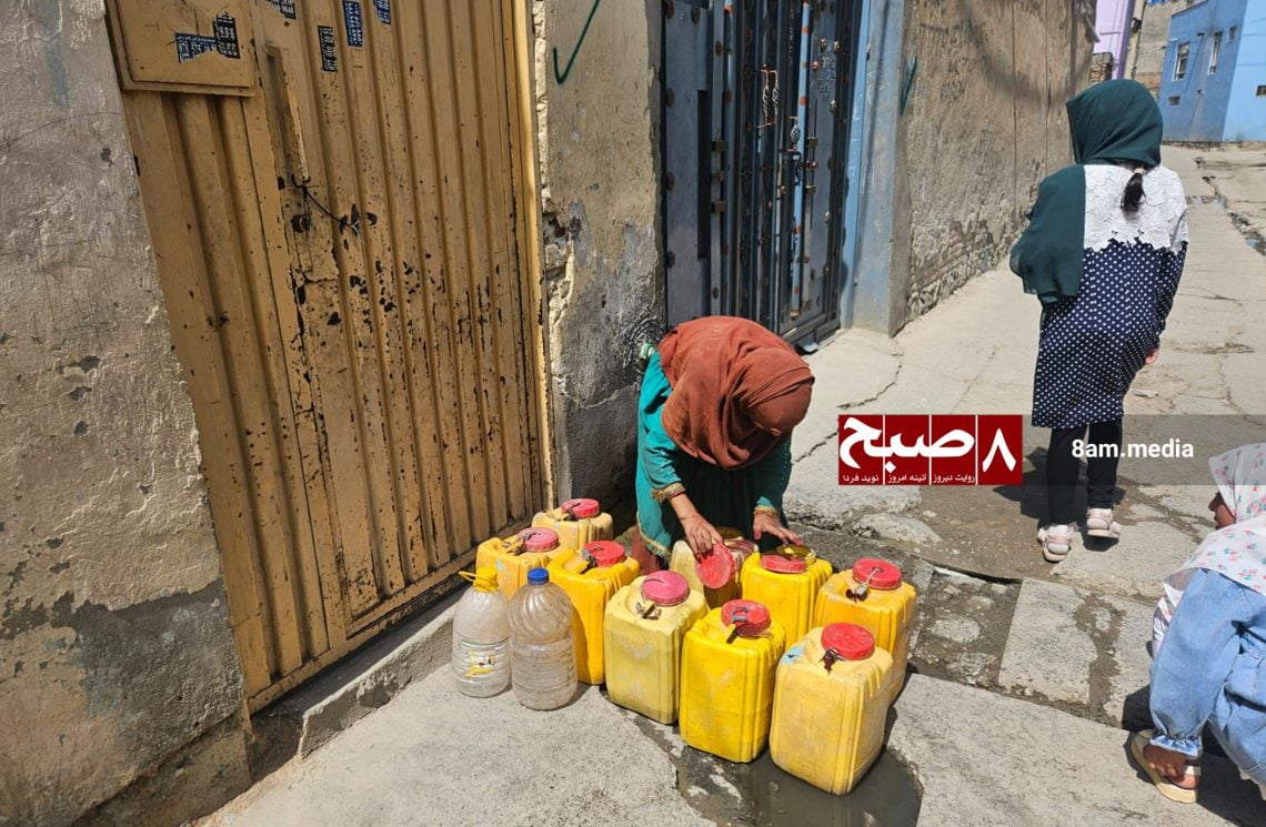 A woman organizes water containers on a Kabul street as residents face daily challenges accessing clean drinking water.