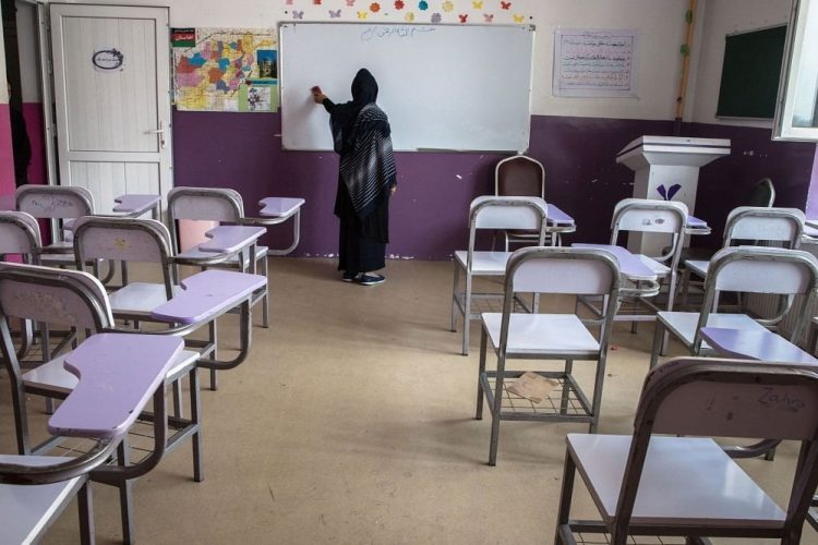 A female teacher writes on the whiteboard in an empty Afghan classroom, reflecting the fear and isolation many women educators face under Taliban rule. (Photo Credit: Ravizan)