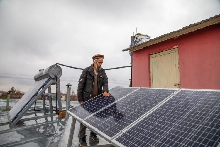 A man inspects solar panels on a rooftop as part of UNDP's clean energy initiative that has brought electricity to hundreds of health centers and thousands of vulnerable families across Afghanistan. (Photo Credit: UNDP)