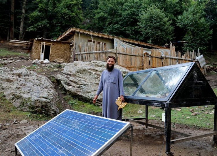 A man stands beside solar panels and a greenhouse at a rural facility in Afghanistan, representing the UN's clean energy initiative that has brought sustainable power to thousands of locations across the country. (Photo Credit: UNDPaf/X@)