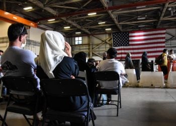 Attendees at an event organized by AfghanEvac, an advocacy group supporting Afghan refugees and Special Immigrant Visa holders, listen to speakers beneath an American flag. (Photo Credit: AfghanEvac)