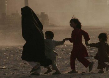 A woman walks with children through a dusty street in Afghanistan, where more than two million refugees have returned in 2025 amid deteriorating humanitarian conditions and severe restrictions on women's rights. (Photo Credit: UNAMA)