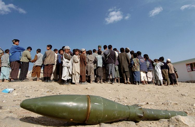 Civilians gather near an unexploded ordnance in Afghanistan as the United Nations warns of escalating mine-related casualties due to reduced funding for mine-action programs. (Photo Credit: AFP)