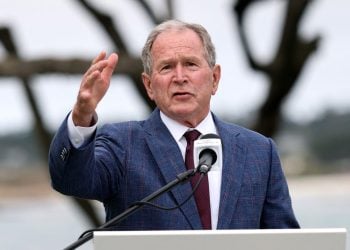 Former President George W. Bush speaks at a podium during an outdoor event, gesturing while addressing migration and refugee policies that have impacted Afghan allies and other immigrants. (Photo Credit: GETTY IMAGES VIA AFP)