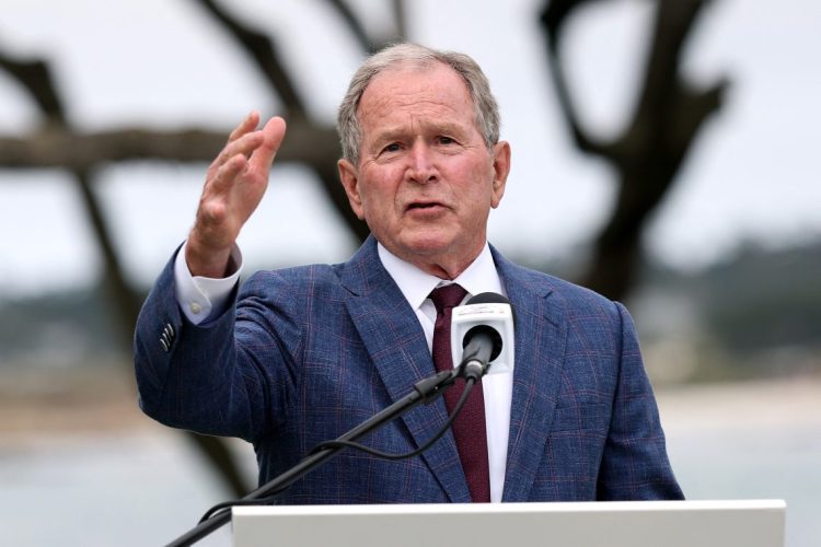 Former President George W. Bush speaks at a podium during an outdoor event, gesturing while addressing migration and refugee policies that have impacted Afghan allies and other immigrants. (Photo Credit: GETTY IMAGES VIA AFP)