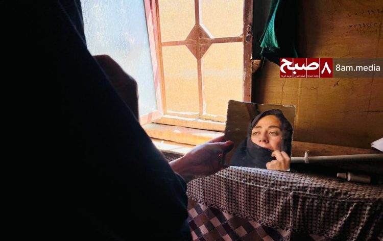 A woman looks at her reflection inside her home, symbolizing the isolation, loss of hope, and ongoing restrictions faced by women under Taliban rule. (Photo Credit: 8am.media)
