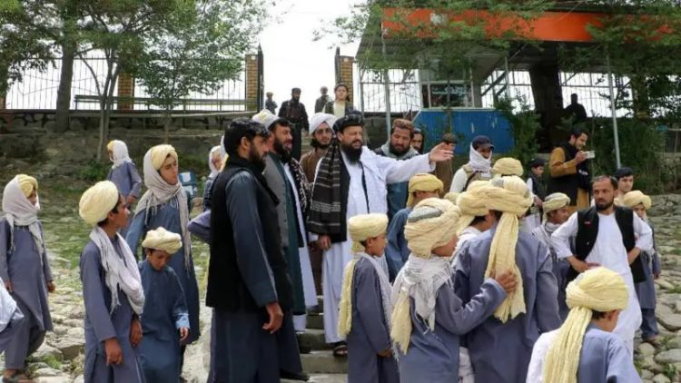 Taliban officials stand with children wearing traditional attire at what appears to be a state-run facility in Afghanistan, amid concerns about the closure of private orphanages and transfer of children to government control. (Photo Credit: MEW_GOV_AF)