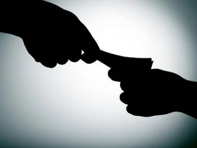 A silhouetted hand passes money to another hand, symbolizing bribery and corruption in government services. (Photo Credit: Shutterstock)