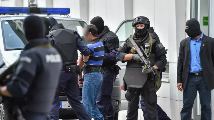 Heavily armed Austrian police officers escort a handcuffed suspect outside a building during a counterterrorism operation. (Photo Credit: AFP)