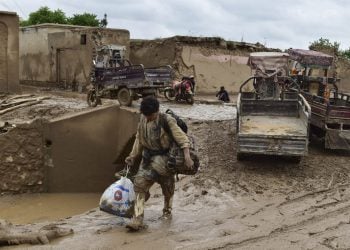Mud-covered man carrying bag, flooded Afghan village (Photo Credit: AFP)