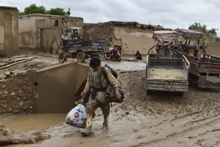 Mud-covered man carrying bag, flooded Afghan village (Photo Credit: AFP)