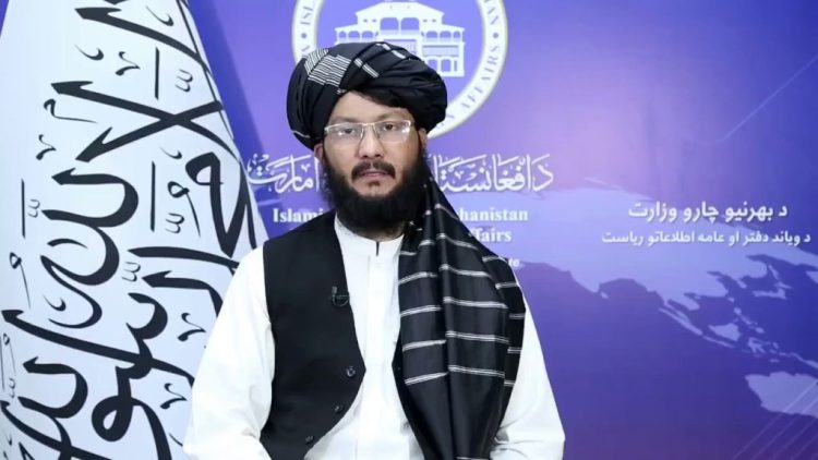 Taliban spokesperson sits beside group flag during statement (Photo Credit: Social Media)