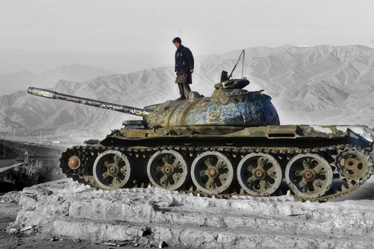 A man stands atop a weathered tank overlooking Afghanistan's rugged mountains, symbolizing decades of conflict and failed state-building. (Photo credit: Getty Images)